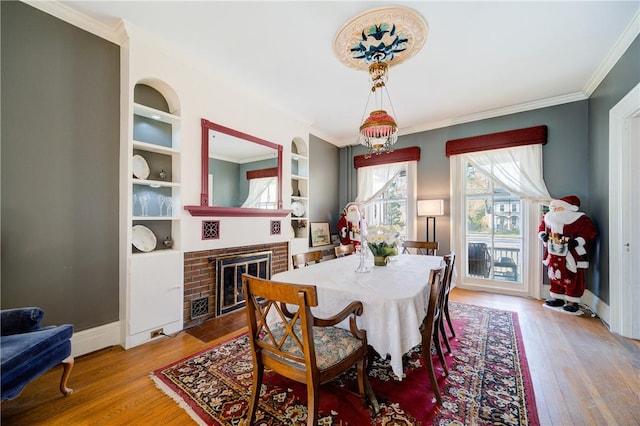 dining room with a brick fireplace, crown molding, built in features, and hardwood / wood-style flooring