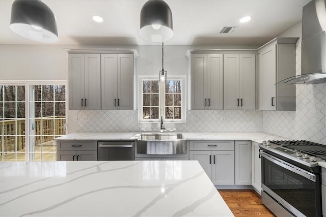 kitchen with appliances with stainless steel finishes, decorative light fixtures, wall chimney exhaust hood, and gray cabinetry