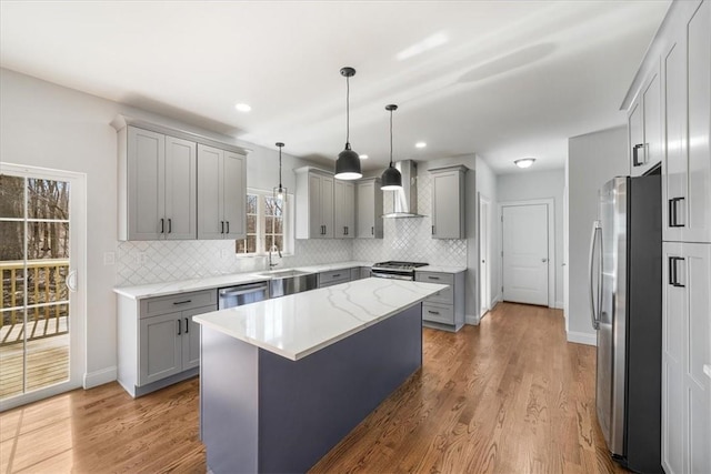 kitchen featuring hardwood / wood-style floors, wall chimney range hood, gray cabinets, a kitchen island, and stainless steel appliances