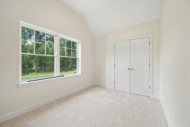 unfurnished bedroom featuring light colored carpet, vaulted ceiling, and a closet