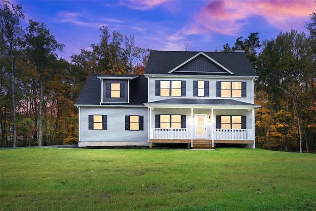 back house at dusk featuring a lawn and covered porch