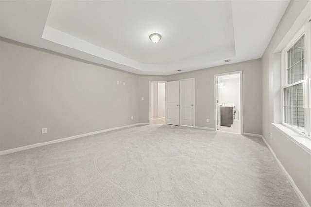 unfurnished bedroom featuring light carpet, a tray ceiling, and ensuite bath