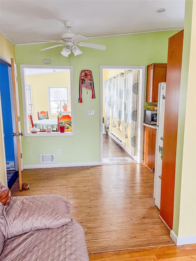 bedroom featuring ceiling fan, a baseboard heating unit, and light wood-type flooring