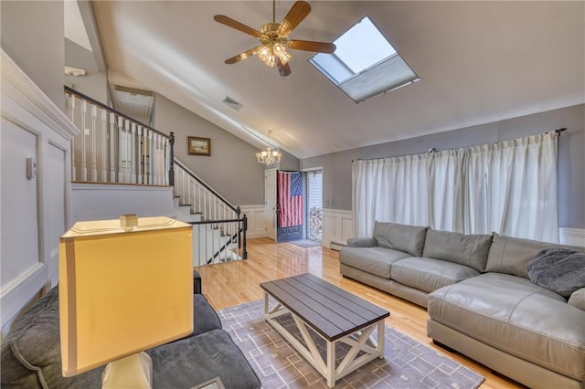 living room with lofted ceiling with skylight, ceiling fan with notable chandelier, and hardwood / wood-style flooring