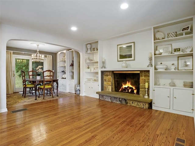 unfurnished living room featuring a fireplace, light hardwood / wood-style flooring, a chandelier, and built in shelves