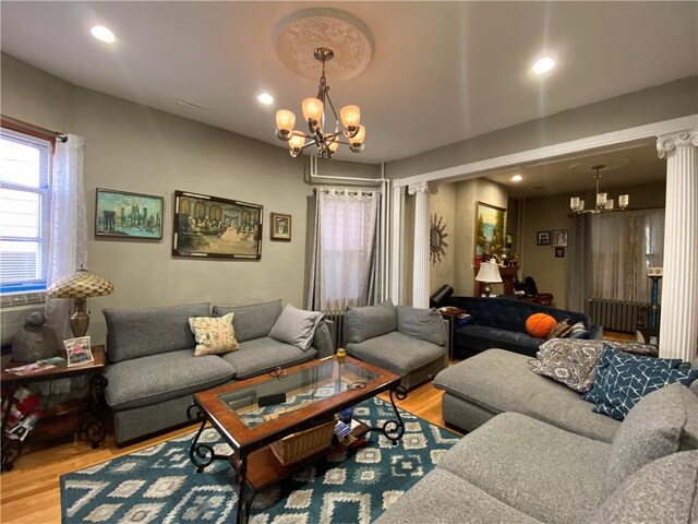 living room featuring ornate columns, wood-type flooring, radiator heating unit, and a chandelier