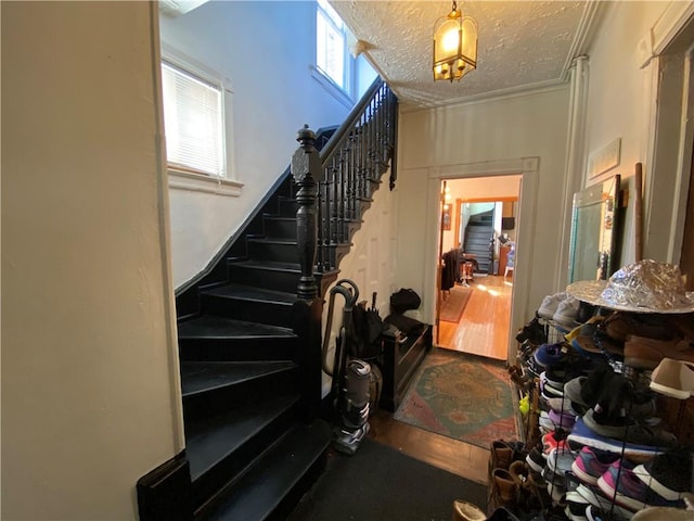 staircase featuring wood-type flooring, a textured ceiling, and ornamental molding