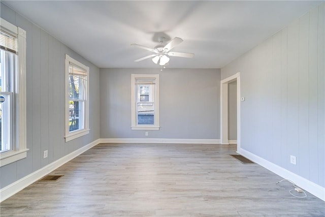 spare room with ceiling fan, wooden walls, and light hardwood / wood-style flooring