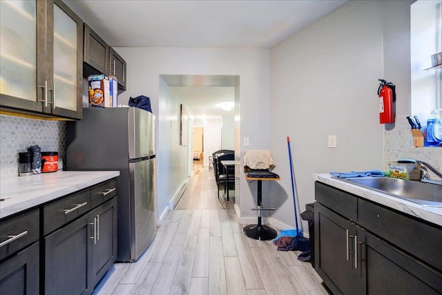 kitchen with backsplash, sink, light wood-type flooring, dark brown cabinetry, and stainless steel refrigerator