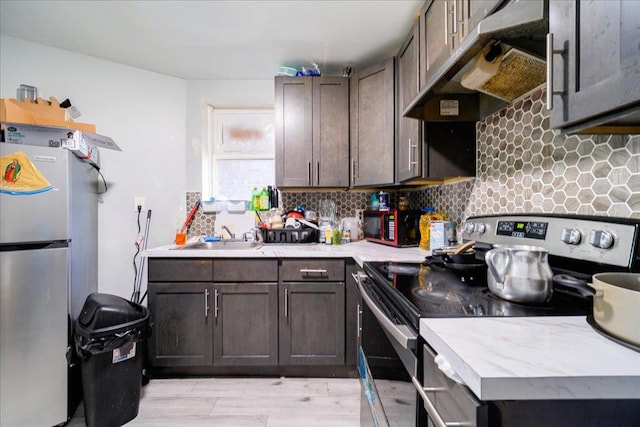 kitchen with appliances with stainless steel finishes, tasteful backsplash, extractor fan, sink, and light hardwood / wood-style flooring