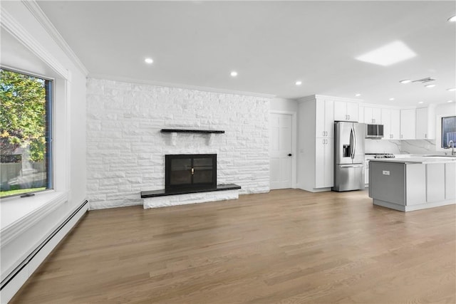 unfurnished living room featuring a stone fireplace, light wood-type flooring, crown molding, and a baseboard heating unit