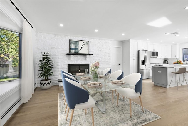 dining room with sink, crown molding, light hardwood / wood-style flooring, a fireplace, and baseboard heating