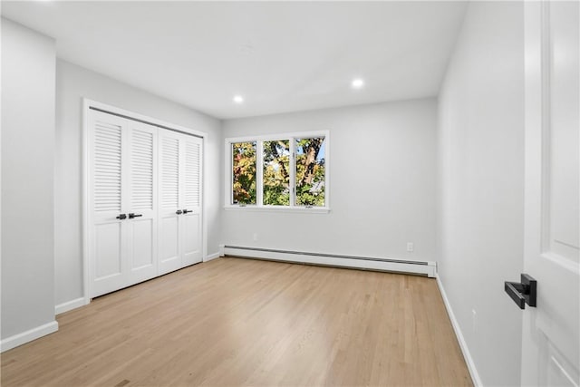 unfurnished bedroom featuring baseboard heating, a closet, and light hardwood / wood-style flooring