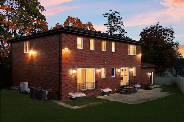 back house at dusk with a lawn, cooling unit, and a patio