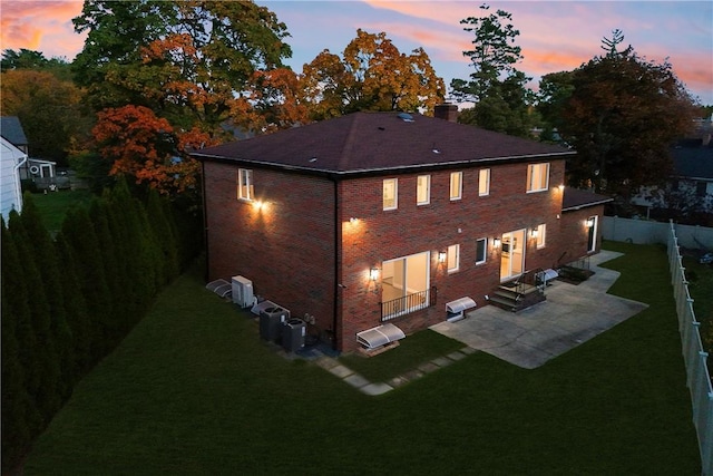 back house at dusk featuring a yard, central AC, and a patio area