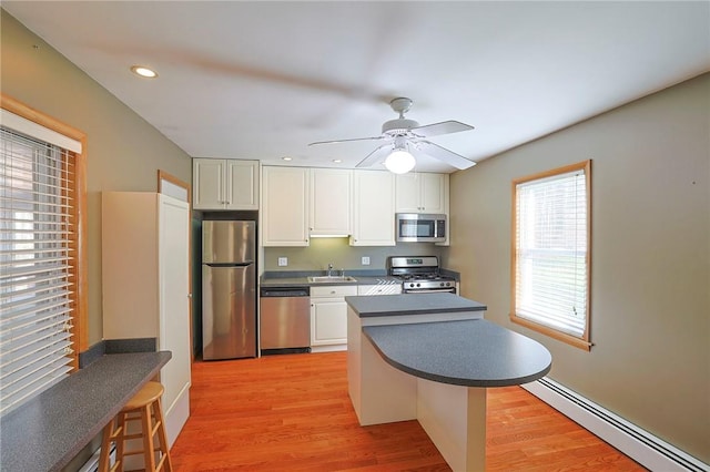 kitchen featuring appliances with stainless steel finishes, a breakfast bar, ceiling fan, a baseboard heating unit, and light hardwood / wood-style flooring