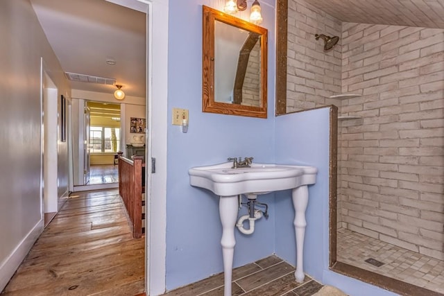 bathroom with hardwood / wood-style floors, a tile shower, and lofted ceiling