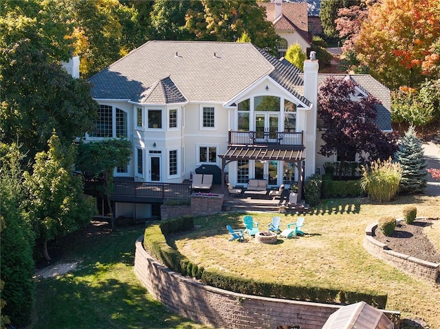 back of property featuring a lawn, a balcony, an outdoor living space with a fire pit, and a patio