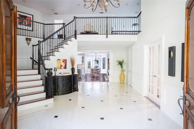 foyer entrance with french doors, an inviting chandelier, crown molding, tile patterned flooring, and a towering ceiling