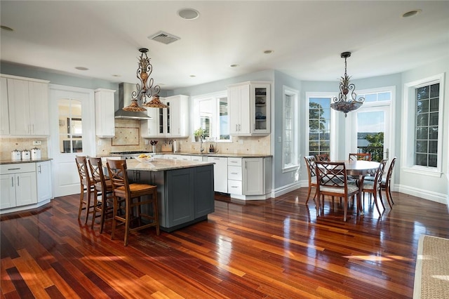 kitchen with dark hardwood / wood-style floors, white cabinets, a healthy amount of sunlight, and wall chimney range hood