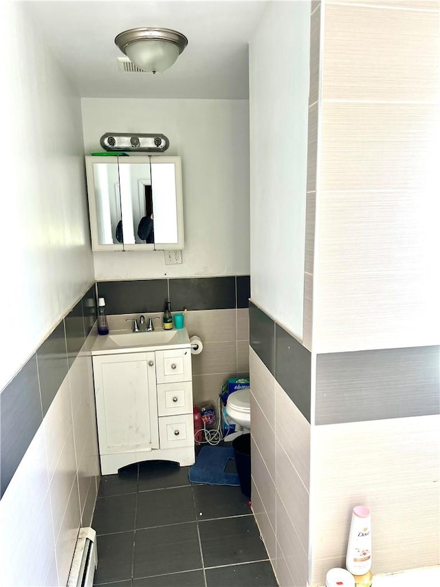 bathroom featuring a baseboard radiator, tile patterned flooring, toilet, vanity, and tile walls