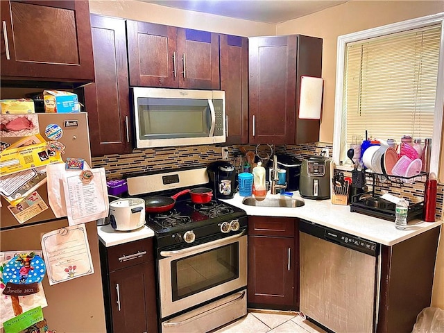 kitchen with backsplash, sink, light tile patterned floors, and appliances with stainless steel finishes