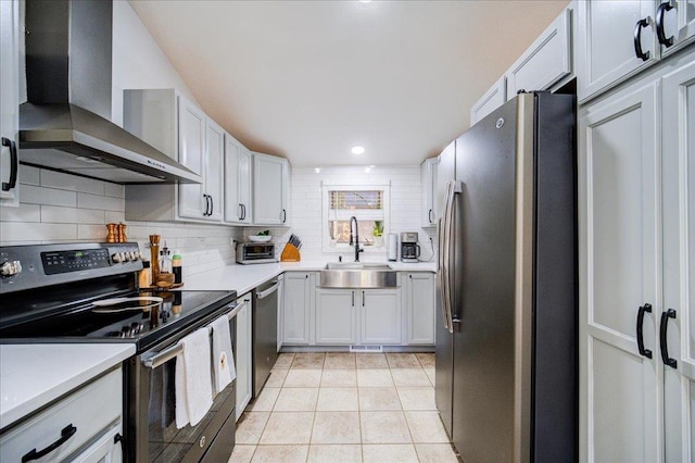 kitchen with sink, wall chimney exhaust hood, stainless steel appliances, light tile patterned floors, and white cabinets