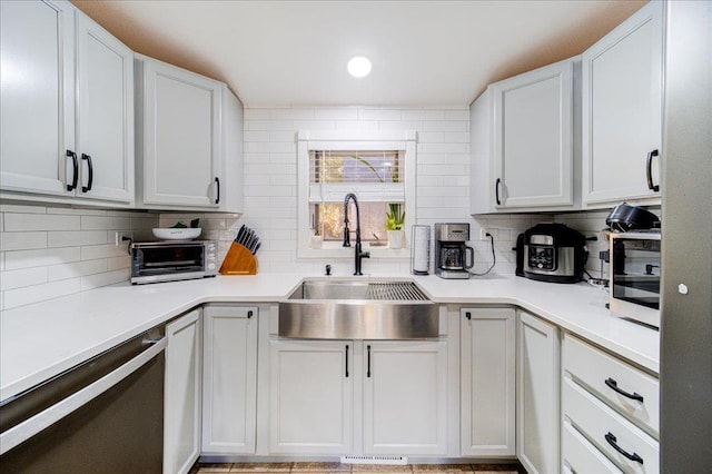 kitchen with stainless steel dishwasher, white cabinetry, sink, and tasteful backsplash