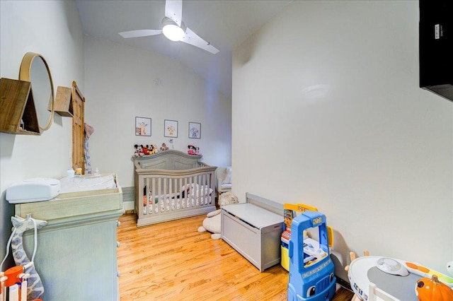 bedroom featuring hardwood / wood-style flooring, ceiling fan, vaulted ceiling, and a nursery area