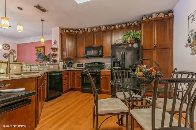 kitchen featuring light stone counters, sink, black appliances, light hardwood / wood-style floors, and hanging light fixtures