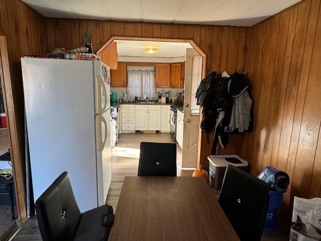 kitchen with sink, light hardwood / wood-style flooring, wood walls, white fridge, and stainless steel stove