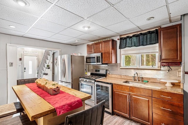 kitchen with sink, beverage cooler, light hardwood / wood-style floors, decorative backsplash, and appliances with stainless steel finishes