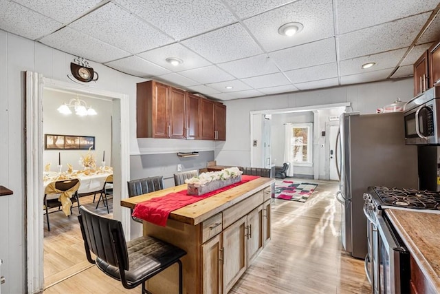 kitchen with pendant lighting, a paneled ceiling, light hardwood / wood-style flooring, appliances with stainless steel finishes, and butcher block countertops