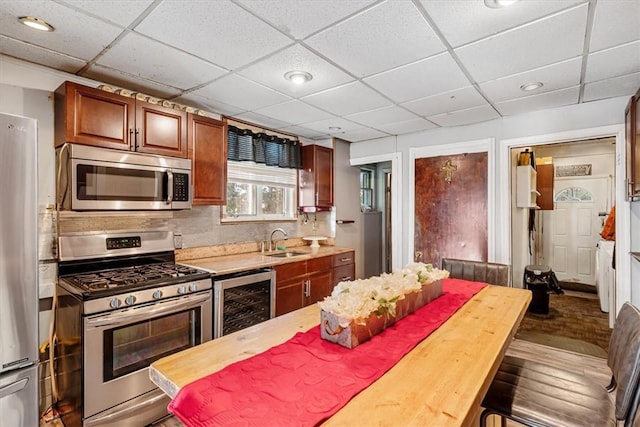 kitchen featuring a paneled ceiling, wooden counters, sink, stainless steel appliances, and beverage cooler