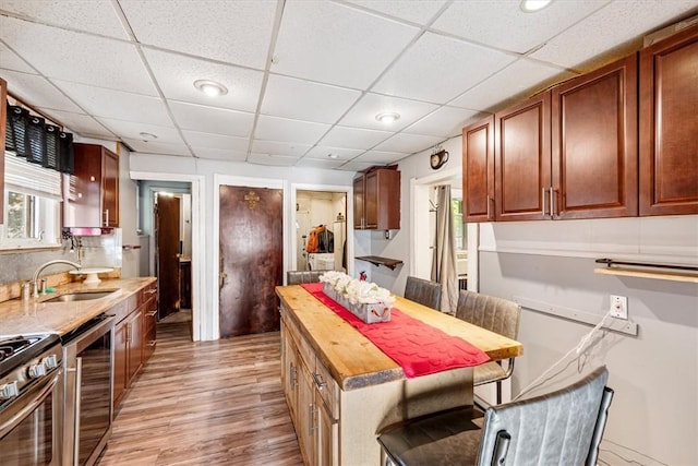 kitchen featuring a drop ceiling, a kitchen breakfast bar, sink, and light hardwood / wood-style flooring