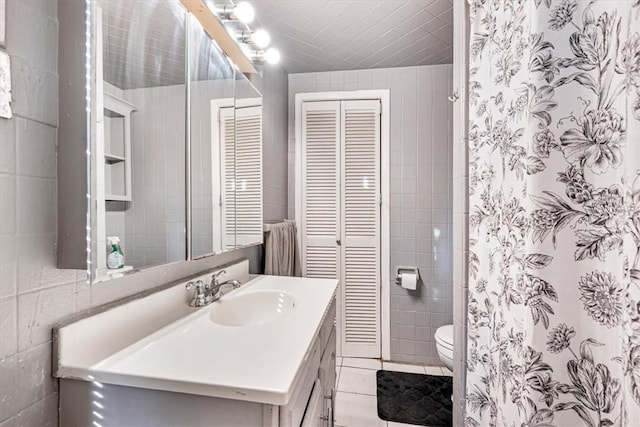 bathroom featuring tile patterned floors, vanity, toilet, and tile walls