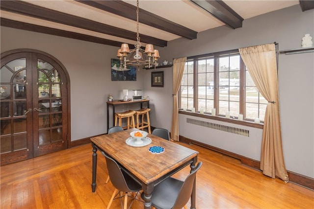 dining area featuring radiator heating unit, french doors, an inviting chandelier, beamed ceiling, and light hardwood / wood-style floors