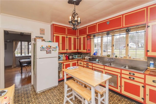 kitchen with decorative backsplash, dark wood-type flooring, stainless steel counters, white refrigerator, and a notable chandelier