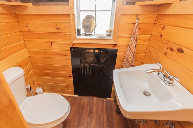 bathroom featuring toilet, wood walls, hardwood / wood-style floors, and sink