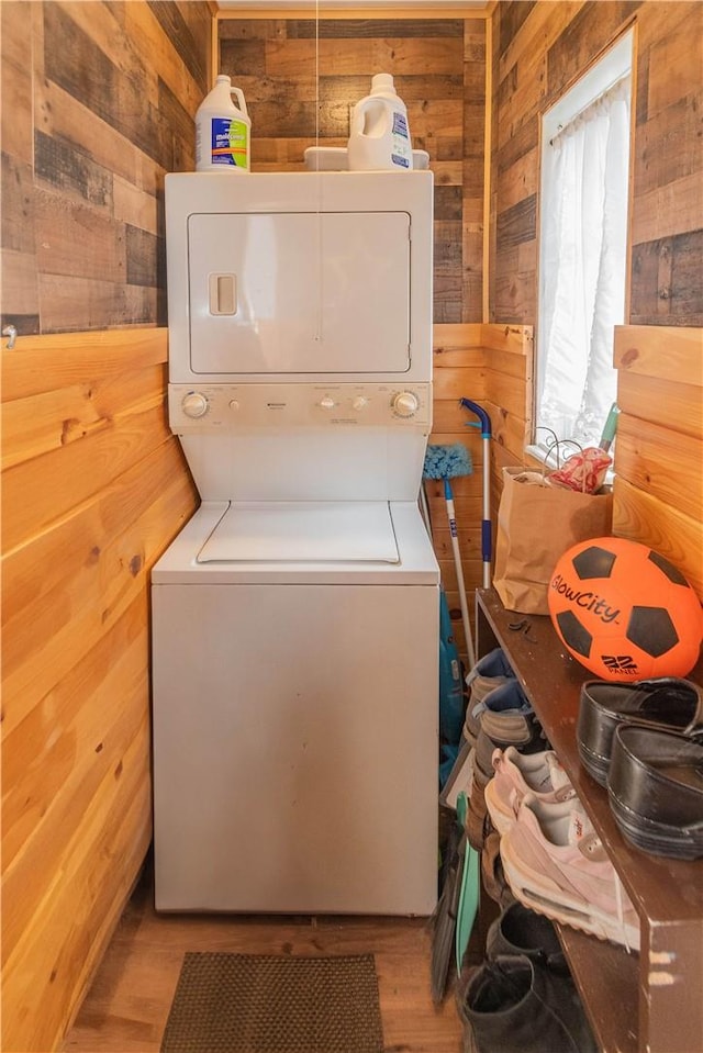 laundry area featuring stacked washer / drying machine, light hardwood / wood-style floors, and wooden walls