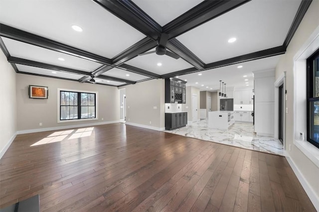 unfurnished living room featuring bar area, coffered ceiling, dark hardwood / wood-style floors, ceiling fan, and beam ceiling