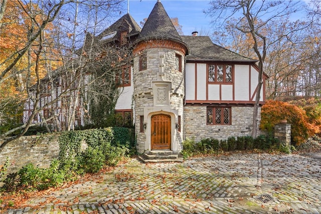 english style home with stone siding, a chimney, and stucco siding