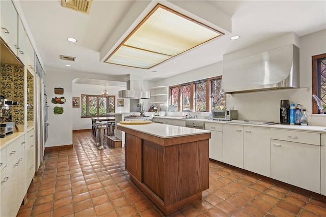 kitchen featuring wall chimney range hood, a kitchen island, stainless steel gas stovetop, island range hood, and white cabinets