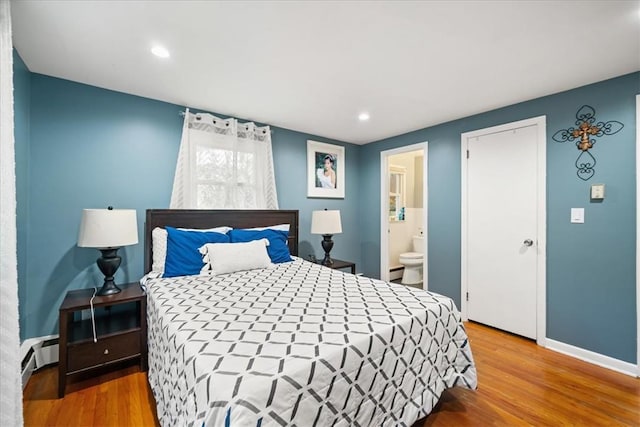 bedroom with baseboard heating, ensuite bathroom, and hardwood / wood-style floors