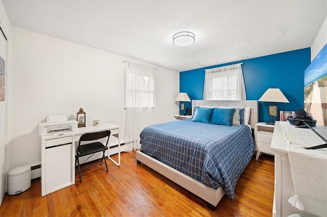 bedroom with baseboard heating, multiple windows, and hardwood / wood-style flooring