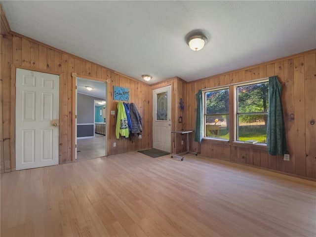 unfurnished room featuring wooden walls, vaulted ceiling, and light wood-type flooring