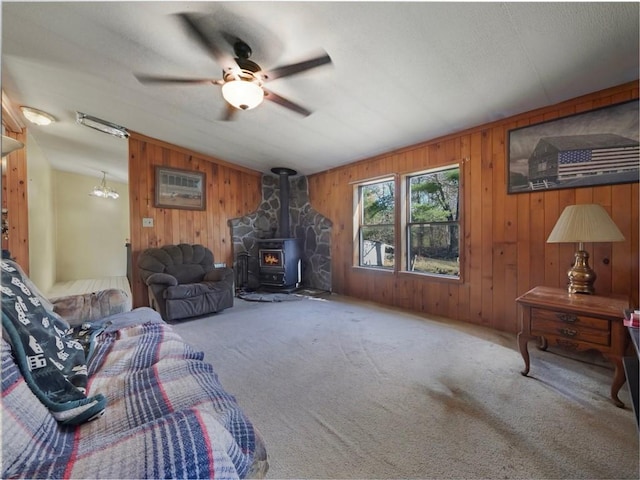 carpeted living room with a wood stove, wooden walls, and ceiling fan