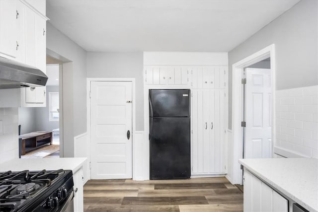 kitchen with white cabinets, decorative backsplash, black refrigerator, and dark wood-type flooring