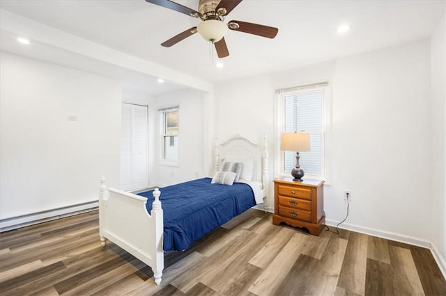 bedroom with a closet, hardwood / wood-style flooring, baseboard heating, and ceiling fan