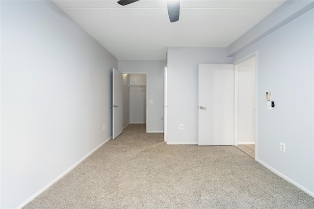 unfurnished bedroom with ceiling fan, a walk in closet, light carpet, and a closet